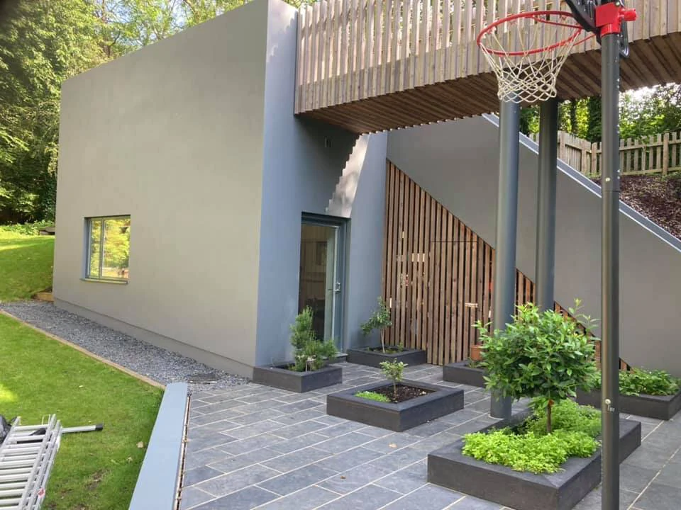 Finished rendered home exterior with timber screening, a raised terrace and planted beds in Swansea